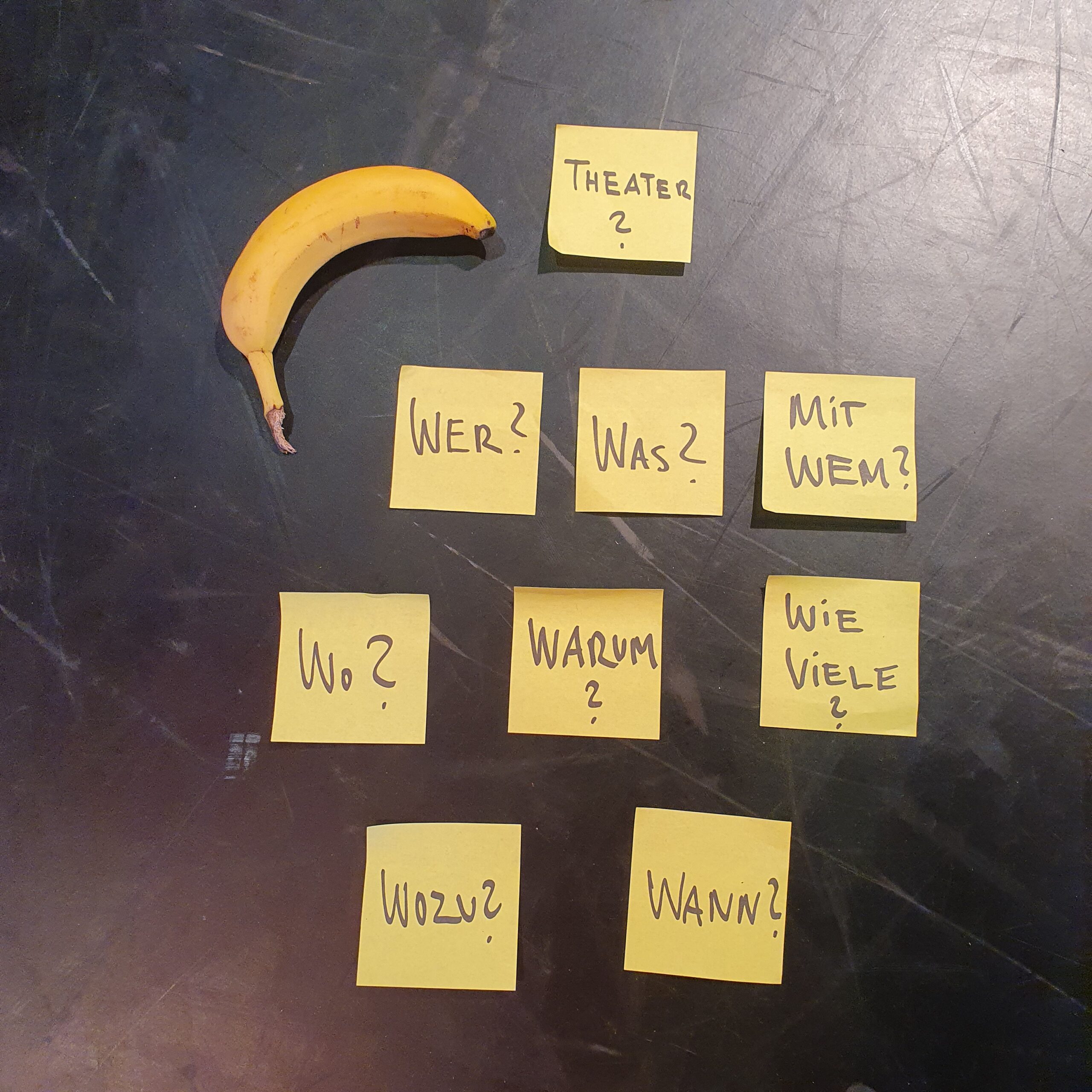 Auf kleinen Zetteln stehen Fragen die für Theater machen wichtig sind. Eine Banane liegt oben rechts dabei.